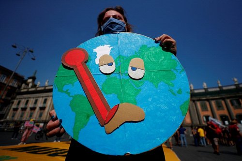 Person hält Plakat auf welchem der Planet Erde mit Fieberthermometer im Mund zu sehen ist.
